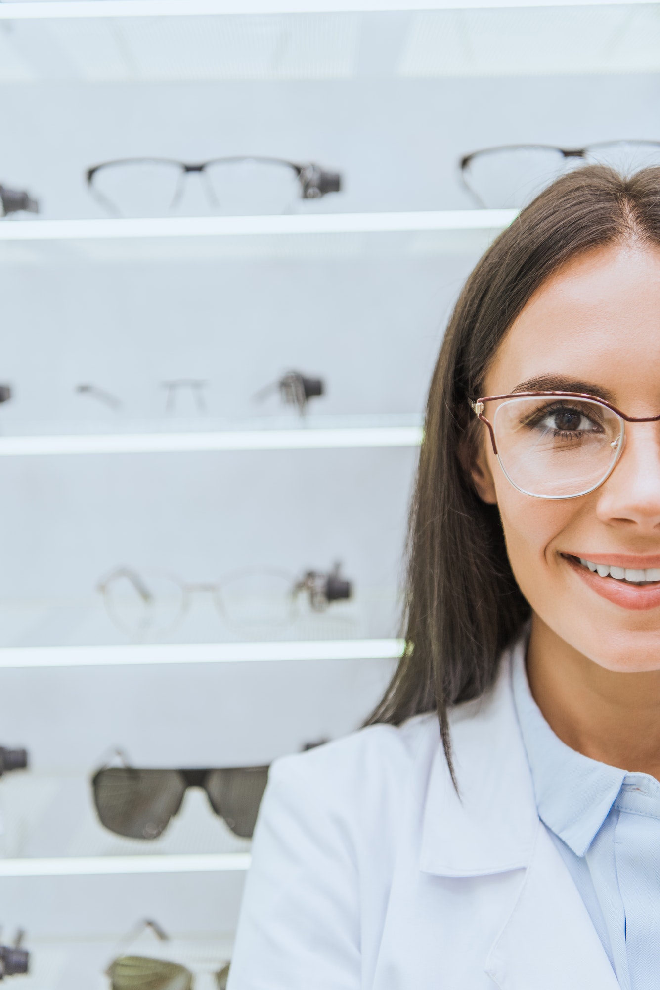 beautiful smiling optician in eyeglasses standing in ophthalmic shop